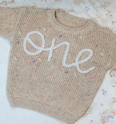 a knitted sweater with the word one written in white thread on top of it