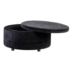 a black ottoman sitting on top of a white floor next to a wooden table with an oval