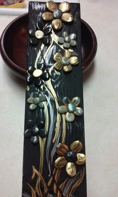 a decorative wooden plate with flowers and leaves painted on the side, sitting on a table next to a bowl