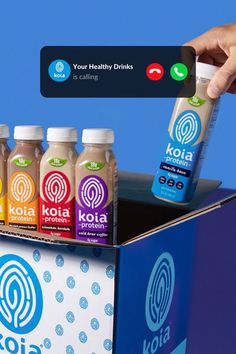 a hand holding a cell phone over a kola drink box