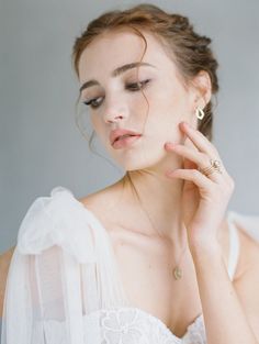 a woman in a white dress is holding her hand up to her face