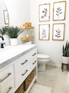 a white bathroom with plants and pictures on the wall