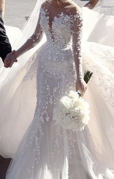 a woman in a white wedding dress holding hands with a man wearing a suit and tie