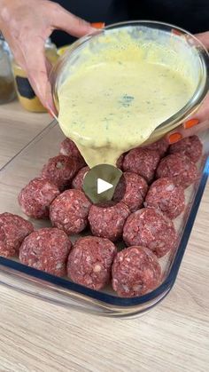 a person pouring sauce on meatballs in a glass dish with other food items nearby