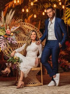 a man and woman posing in front of a wicker chair with flowers on it