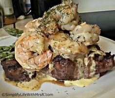 a white plate topped with meat and shrimp covered in gravy next to asparagus