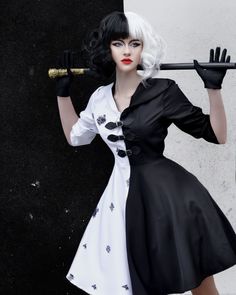 a woman dressed in black and white poses with a cane over her shoulder as she stands against a wall