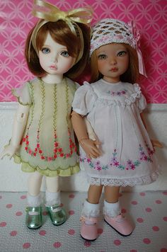 two dolls standing next to each other on a pink and white wallpapered background