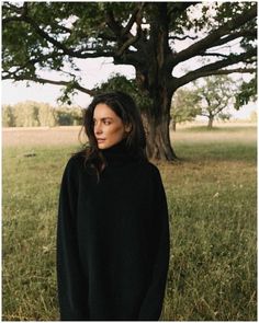 a woman standing in front of a tree wearing a black turtle neck sweater and jeans