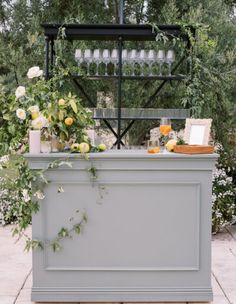 an outdoor bar with flowers and wine glasses on the top, surrounded by greenery