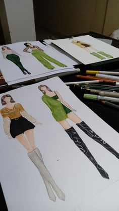 several drawings of women's dresses are on the table next to pencils and crayons