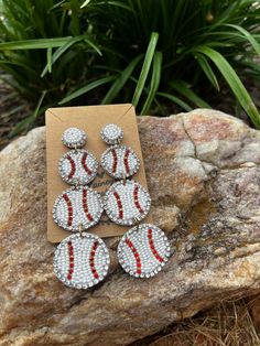 four pairs of baseball beaded earrings sitting on top of a rock