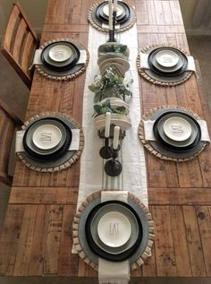 the table is set with black and white plates, silverware, and greenery