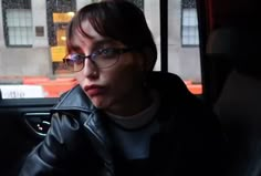 a woman wearing glasses sitting in the back seat of a car