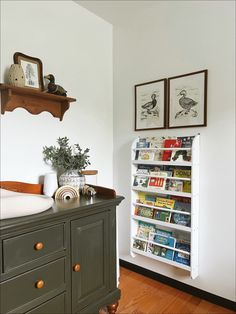 a book shelf in the corner of a room with books on it and pictures above