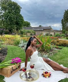 a woman sitting on top of a white towel next to a table filled with fruit