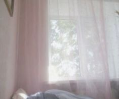 a bed sitting under a window next to a pink curtain