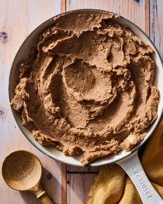 a bowl filled with chocolate frosting next to two wooden spoons