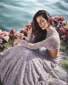 a woman in a purple dress sitting on the ground next to some flowers and water