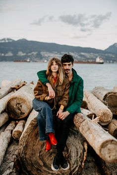 a man and woman sitting on logs by the water