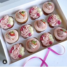 twelve cupcakes with pink frosting and fresh strawberries in a white box