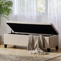 a beige storage bench sitting on top of a wooden floor next to a potted plant