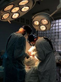 three doctors performing surgery on a baby in an inclosure with light bulbs overhead