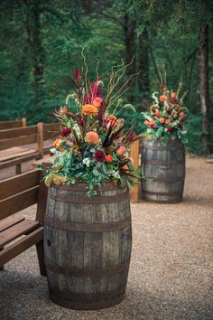 two wooden barrels with flowers and greenery in them sitting on the ground next to a bench