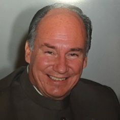 an older man with grey hair smiling at the camera while wearing a priest's uniform