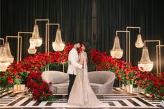 a bride and groom kissing in front of red flowers on a black and white checkered floor