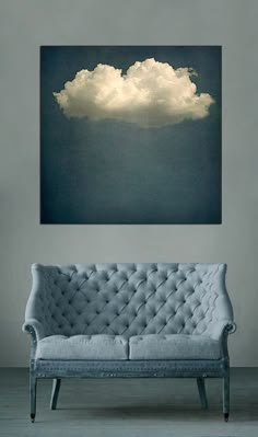 a couch sitting in front of a painting on the wall with clouds floating above it