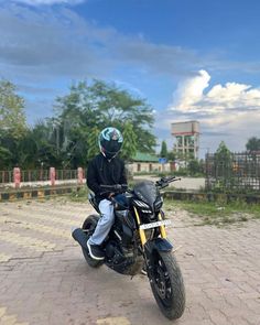 a man riding on the back of a motorcycle down a brick road next to trees