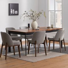 a dining room table with chairs and a vase on top of it in front of a window