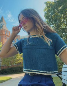 a woman in blue shirt sitting on a bench with her hand to her face and eyeglasses over her eyes