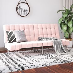 a pink couch sitting on top of a wooden floor next to a potted plant