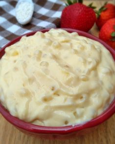 a red bowl filled with mashed potatoes next to strawberries on a checkered table cloth