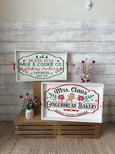 two christmas signs are on display in front of a wooden paneled wall, one is for mrs claus and the other is gingerbread bakery