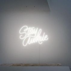 a neon sign that reads stay awhile on it's side in front of a white wall