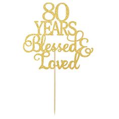 a cake topper with the words 80 years, blessing and loved on it in gold glitter