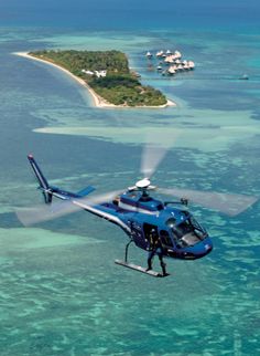 a blue helicopter flying over the ocean with an island in the background