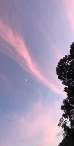 the sky is filled with pink clouds as the sun goes down in the distance behind some trees