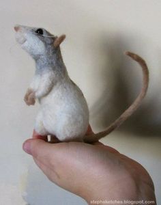 a small toy mouse sitting on top of someone's hand in front of a wall