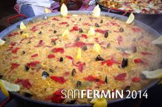 a large pan filled with lots of food on top of a table next to people