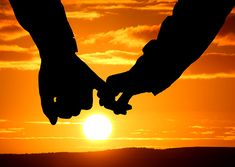 two people holding hands as the sun sets in the background with clouds and orange sky