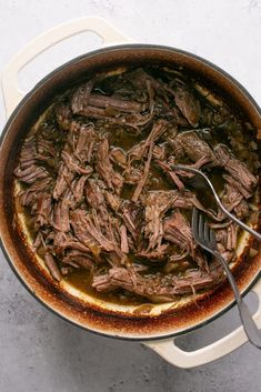 a pot filled with meat and gravy on top of a white countertop