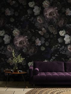 a purple couch sitting in front of a wall with flowers on it and a rug