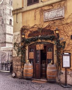 an old building with two wooden barrels in front of it and vines growing on the wall