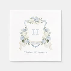 a white square paper napkin with blue flowers and ribbon on the front, in an ornate frame