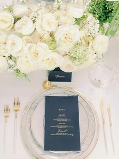 a table setting with white flowers and silverware on the place settings, along with menus