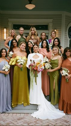 a group of women standing next to each other in front of a white house wearing dresses